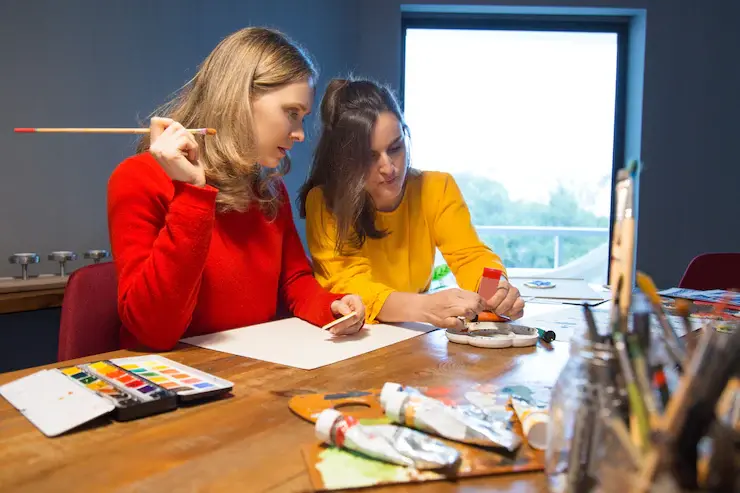 Students working in a design studio with art supplies, computers, and creative projects displayed